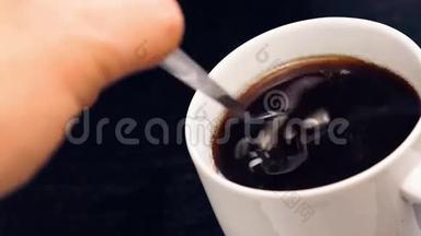 在黑木桌上，用成人手拿<strong>一个勺子</strong>在里面喝一杯黑咖啡